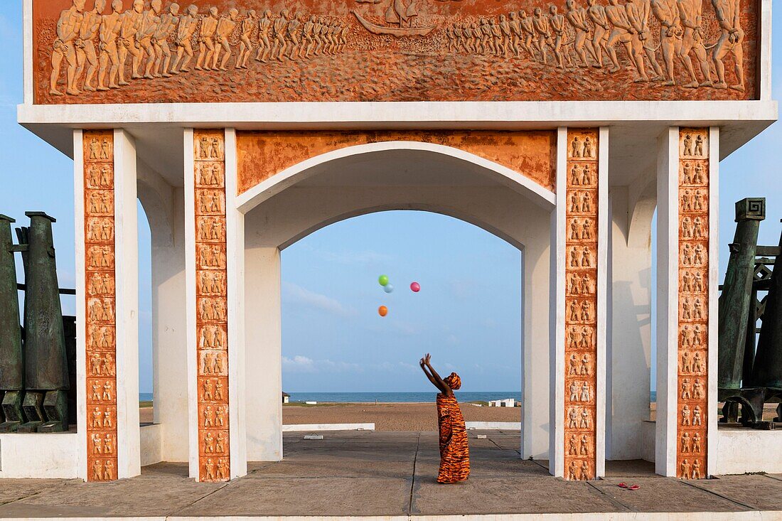 Benin, Ouidah, Frau, die als Zeichen der Freiheit Luftballons steigen lässt, unter dem 1995 von der UNESCO errichteten Tor ohne Wiederkehr, Symbol der Sklaverei