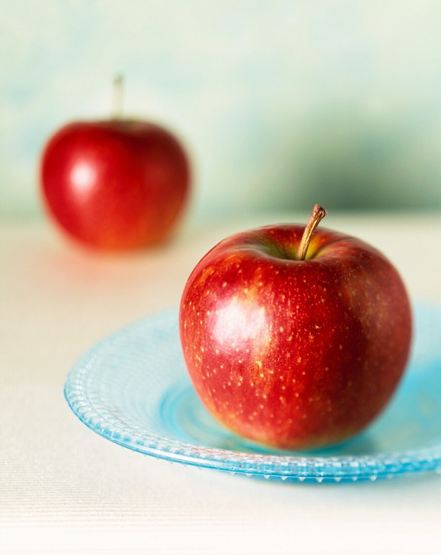 Zwei rote Äpfel, einer im Vordergrund auf blauem Teller