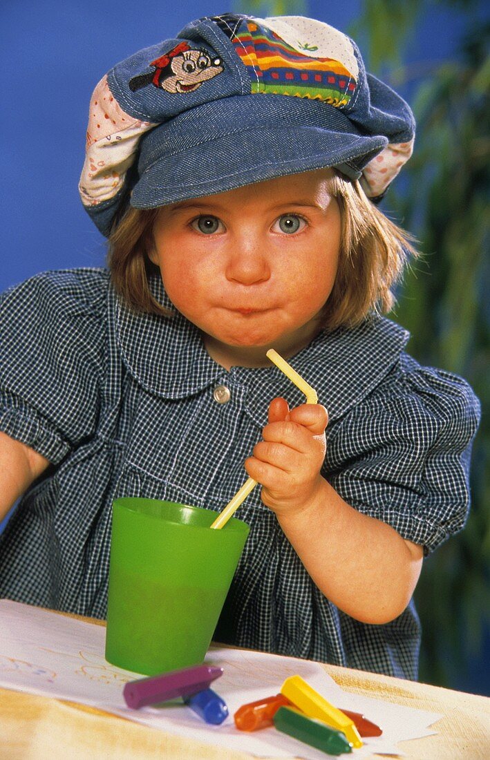Kleines Mädchen mit Saft im grünen Becher mit Strohhalm