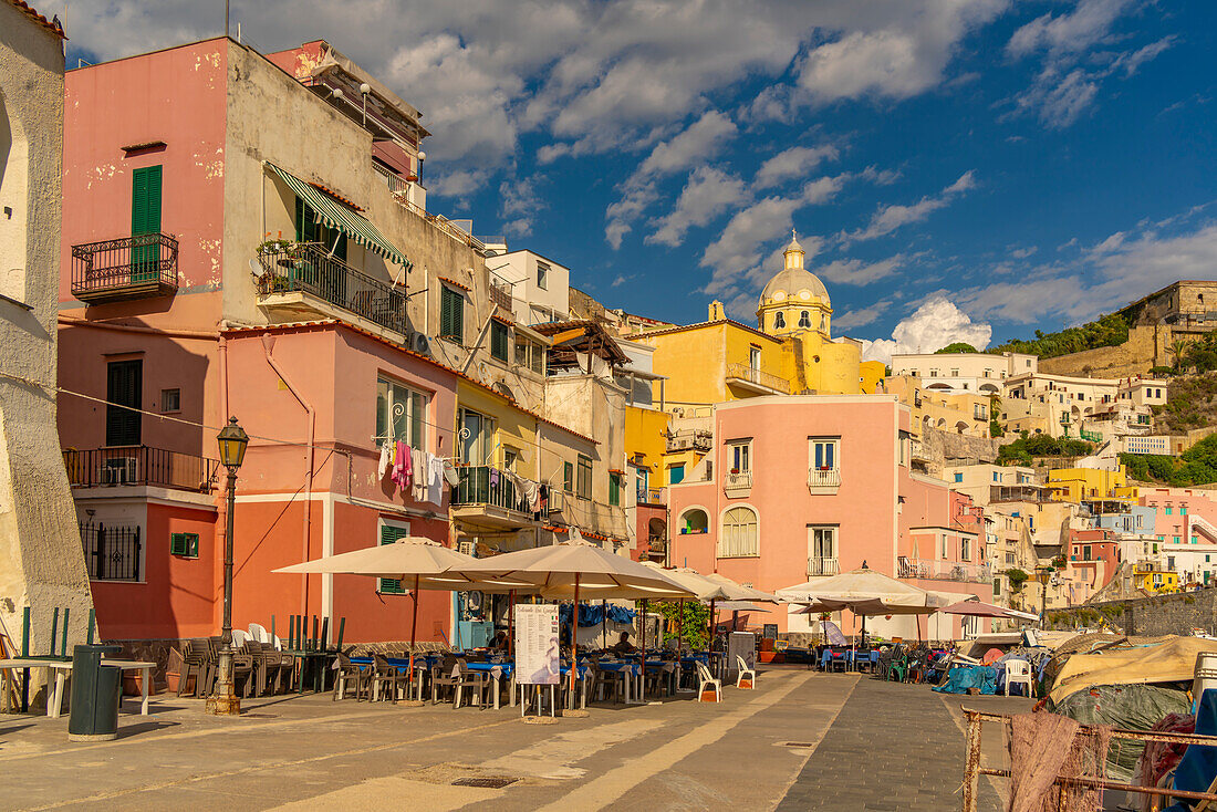 View of restaurant in Marina di Corricella and Church of Santa Maria delle Grazie in background, Procida, Phlegraean Islands, Gulf of Naples, Campania, Southern Italy, Italy, Europe