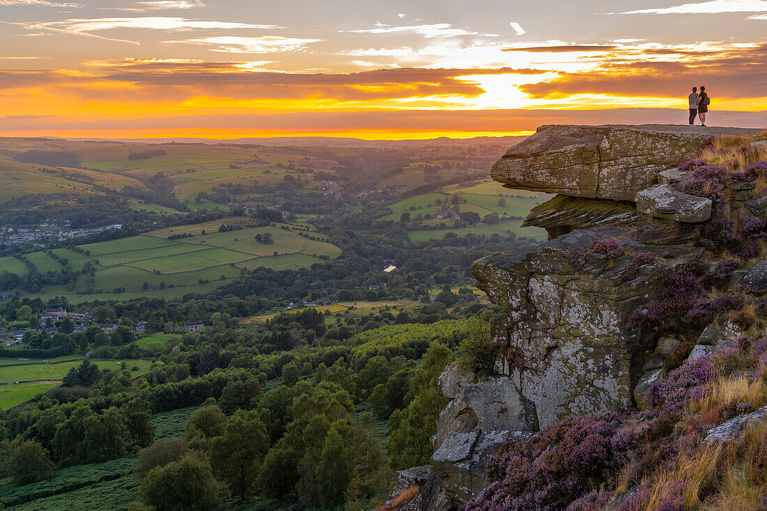 Blick auf einen Mann und eine Frau,die bei Sonnenuntergang die Landschaft von Curbar Edge aus betrachten,Peak District National Park,Baslow,Derbyshire,England,Vereinigtes Königreich,Europa