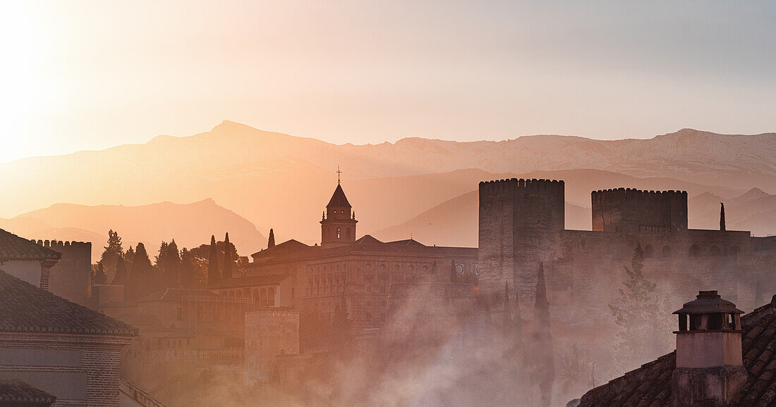 Atmospheric sunrise over the Alhambra, UNESCO World Heritage Site, capturing the historic architecture silhouetted against the golden hues of the Sierra Nevada mountains, Granada, Andalusia, Spain, Europe