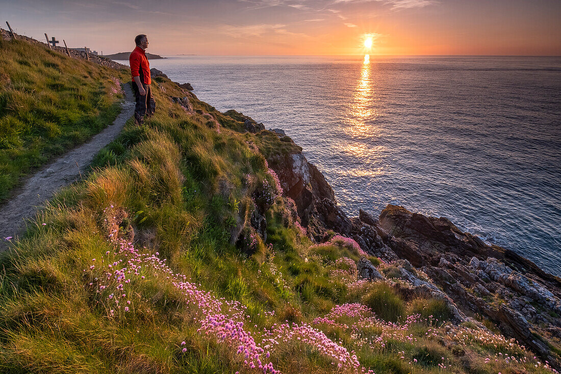 Spaziergänger mit Blick auf das Meer vom Anglesey Coast Path bei Sonnenuntergang im Frühling,nahe Cemaes,Anglesey,Nordwales,Vereinigtes Königreich,Europa