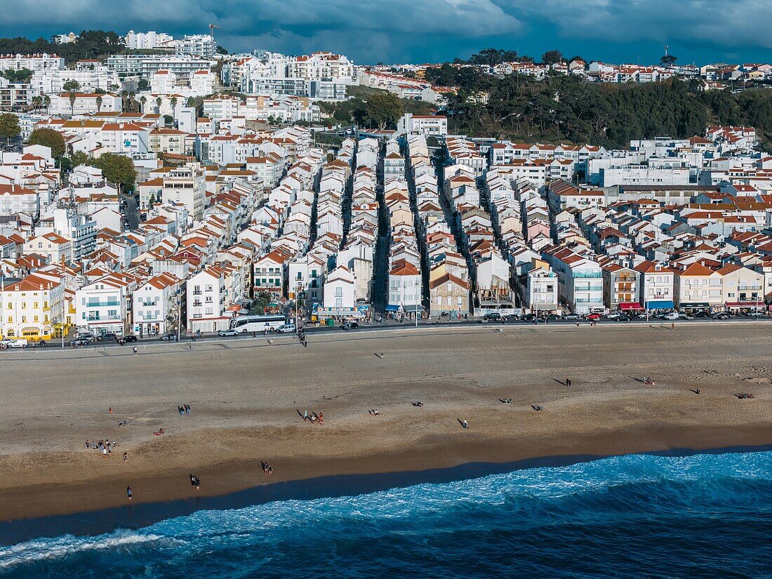 Der belebte Strand,der Reihen von charmanten Häusern mit roten Dächern und Menschen zeigt,die den Sandstrand unter einem klaren Himmel genießen,Nazare,Oeste,Estremadura,Portugal,Europa