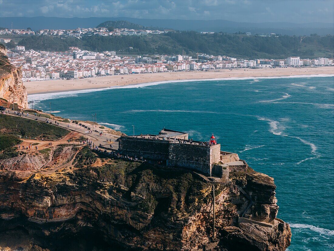 Aerial view of tourists at the historic Sao Miguel Arcanjo lighthouse overlooking Nazare's stunning coastline with giant waves, enjoying spectacular views, Nazare, Oeste, Estremadura, Portugal, Europe