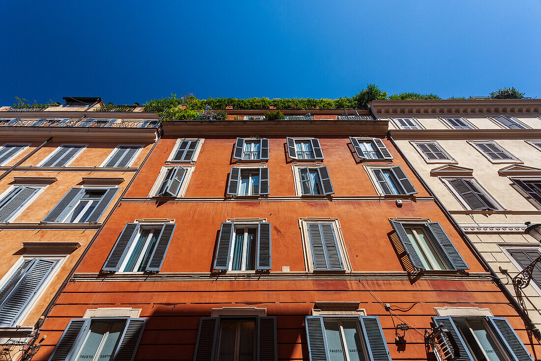 Colorful Roman houses with balconies stretch along Frattina Street beneath a bright blue sky.