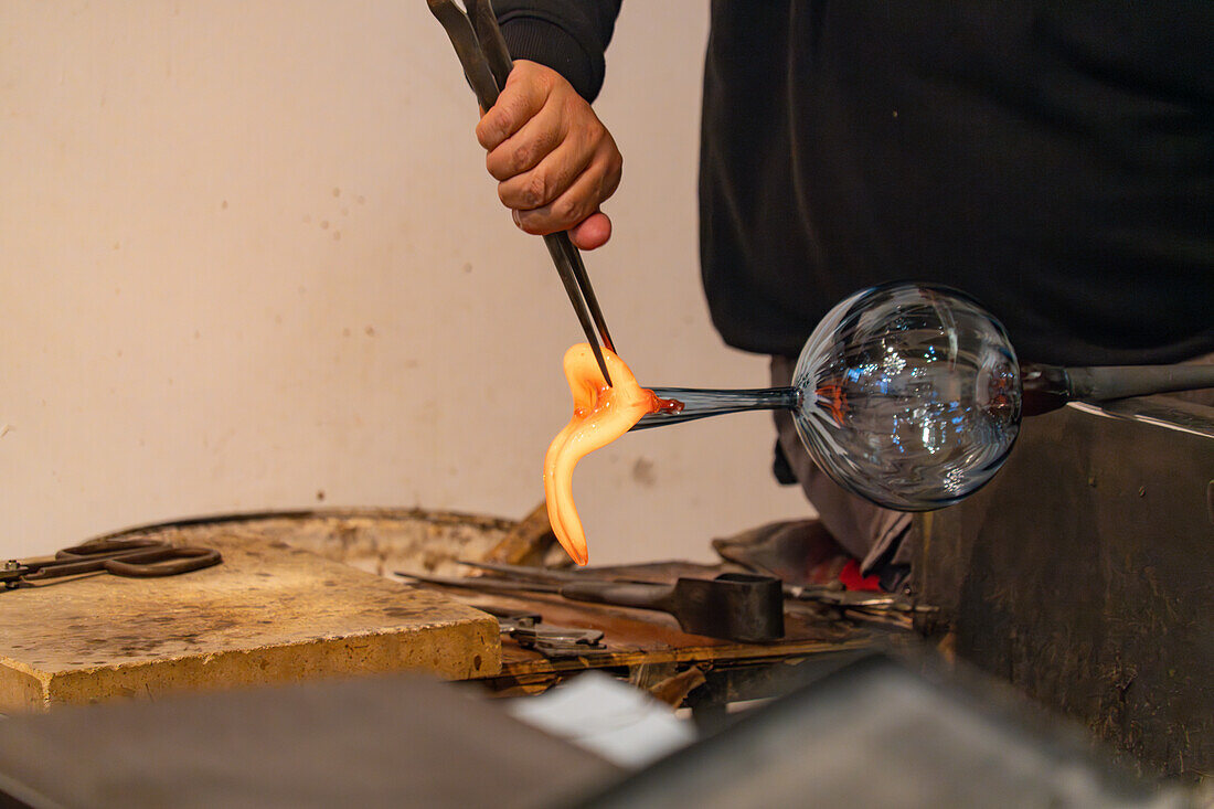 The glassblower shapes a spout for the pitcher with jacks in a glassblowing demonstration in Venice, Italy.