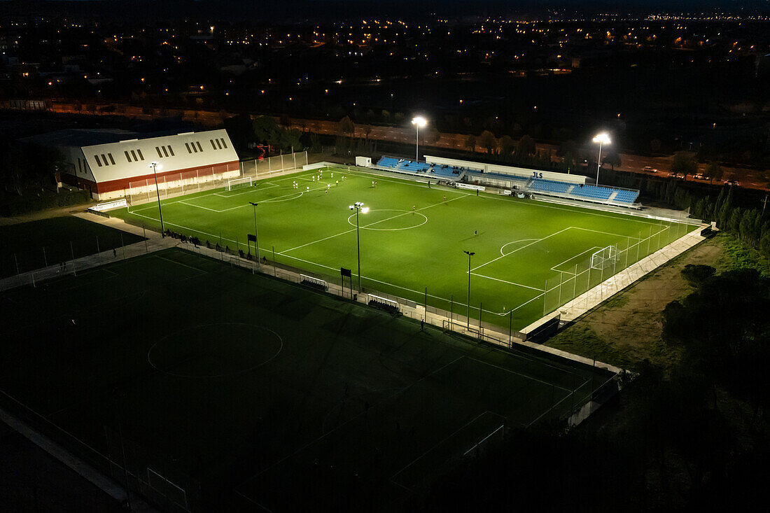 Luftaufnahme eines beleuchteten Amateurfußballplatzes bei Nacht