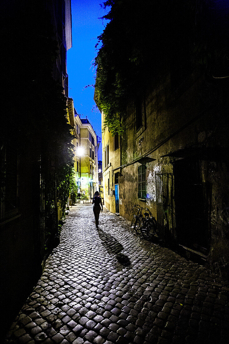 Menschen spazieren im sanften Licht der Nacht über Kopfsteinpflaster in Trastevere und fangen die Essenz des pulsierenden Nachtlebens in Rom ein.