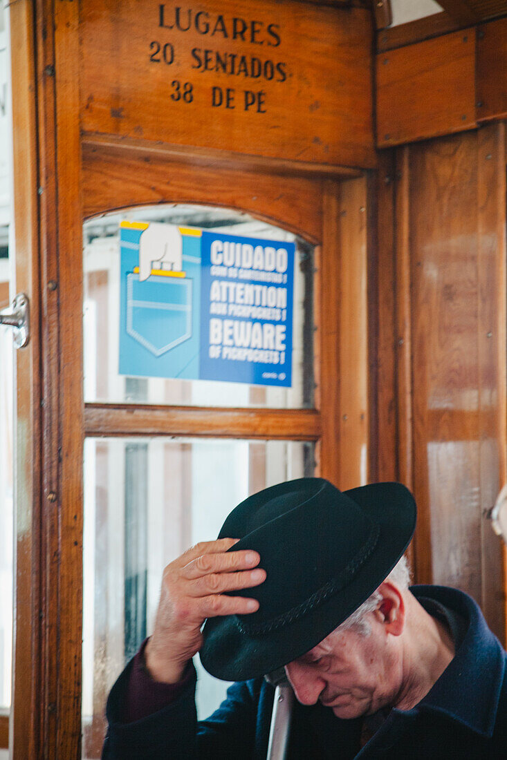 Lisbon, Portugal, March 1 2007, An elderly man wearing a hat sits quietly inside a Lisbon tram as the urban landscape moves outside.