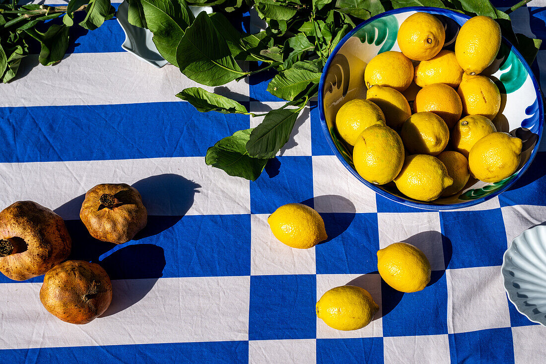 A vibrant display of fresh pomegranates and lemons on a blue checkered tablecloth in Malaga, Spain, creating a lively and Mediterranean feel.