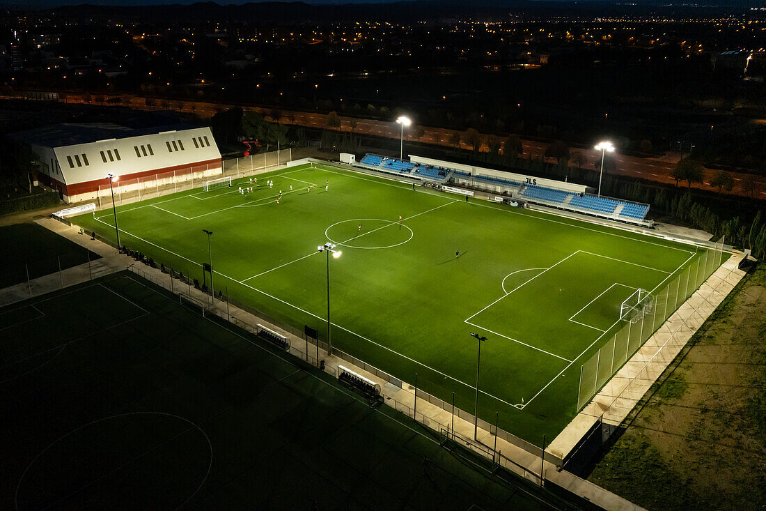 Luftaufnahme eines beleuchteten Amateurfußballplatzes bei Nacht