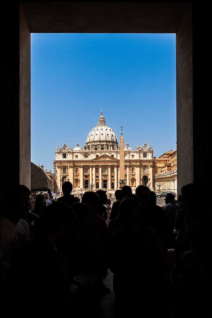 Visitors gather in the foreground while admiring the stunning Saint Peter's Basilica in Vatican City on a clear day.