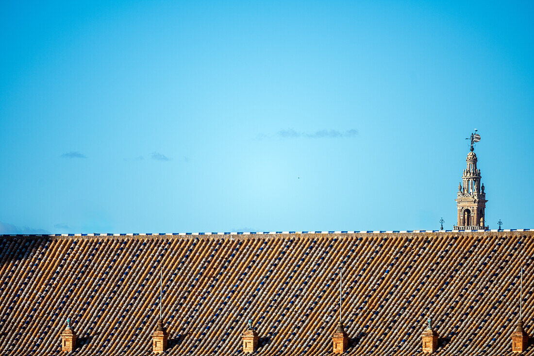 A clear blue sky over a traditional rooftop in Seville, Spain, with the iconic La Giralda tower in the background, capturing the historic charm of the city.