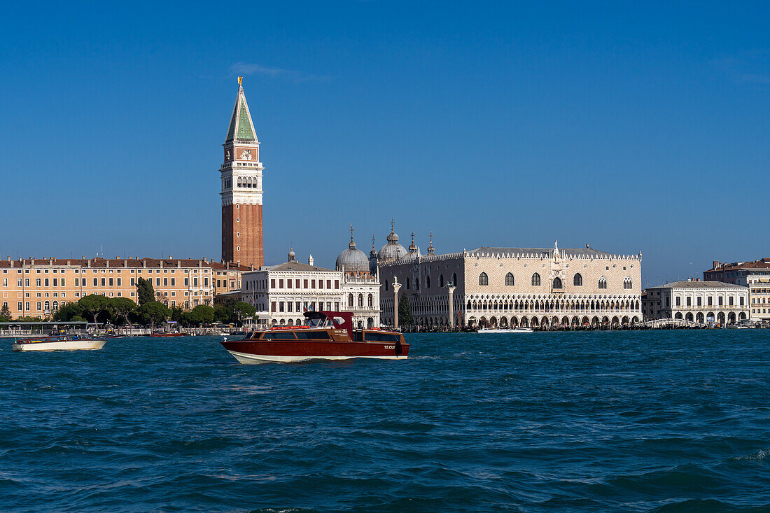 The St. Mark's cathedral bell tower & facade of the Doge's Palace (right) seen from the Giudecca Canal in Venice, Italy. The domes of St. Mark's are seen behind.