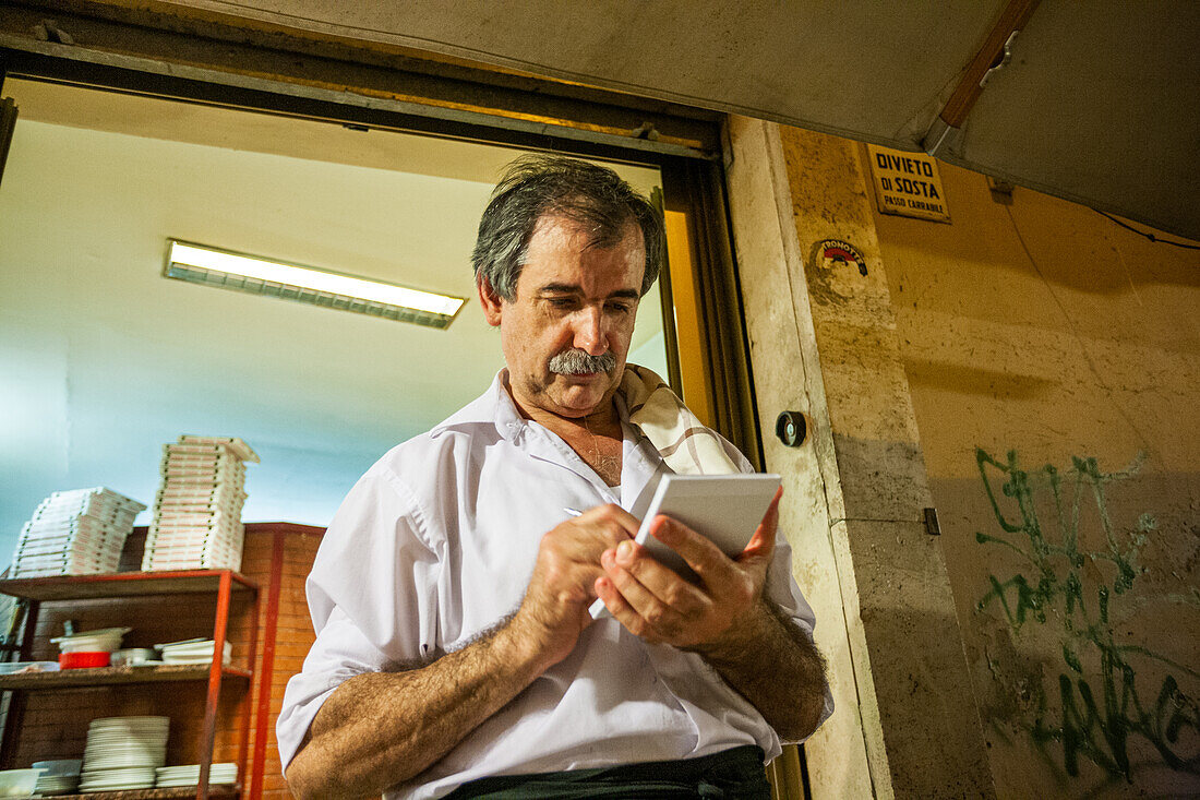 Rome, Italy, July 22 2017, A Roman waiter is busy jotting down orders with a notepad in a lively eatery in Rome while guests enjoy their meals.