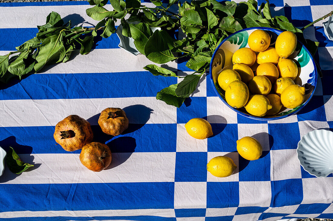 Lebendige Zitronen und Granatäpfel auf einer blau-weiß karierten Tischdecke,die die Essenz einer festlichen Zusammenkunft in Malaga,Spanien,einfängt.