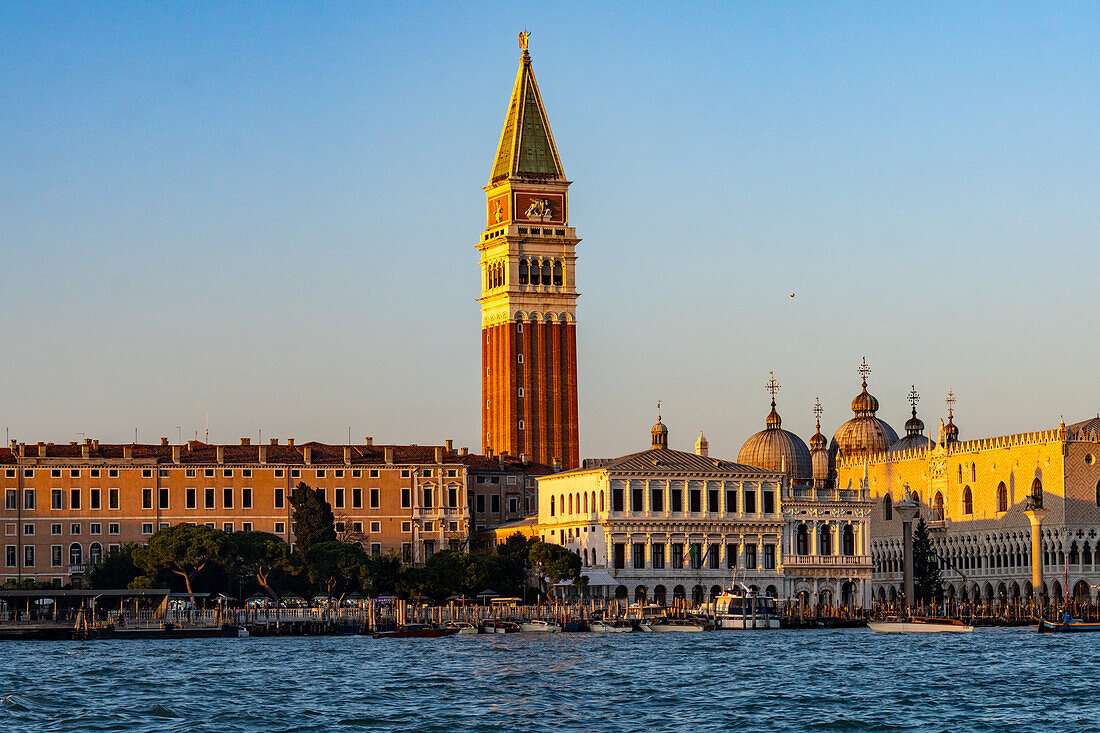 The bell tower & domes of the Basilica of St. Mark with golden light at sunset in Venice, Italy.