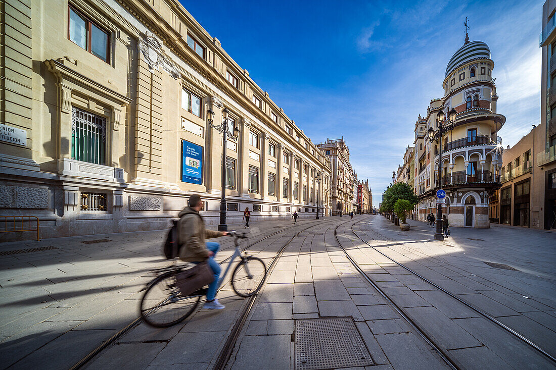 Seville, Spain, Jan 28 2021, A cyclist rides past the picturesque Adriatica Building on Avenida de la Constitucion in Sevilla. The street is lined with stunning architecture under a clear blue sky.