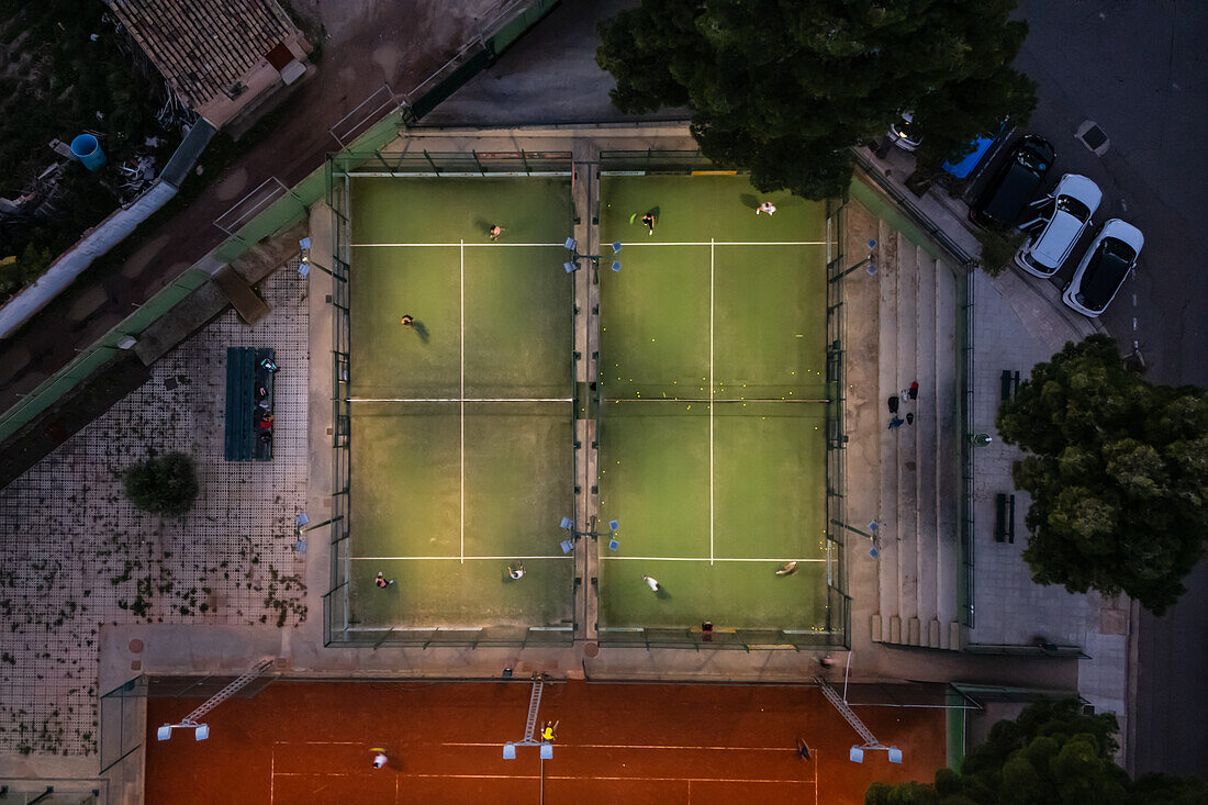 Aerial vertical view of people playing paddle tennis in an illuminated court