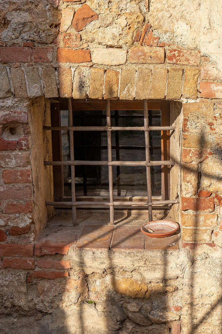 Barred window in a building in the medieval walled town of Monteriggioni, Sienna, Tuscany, Italy.