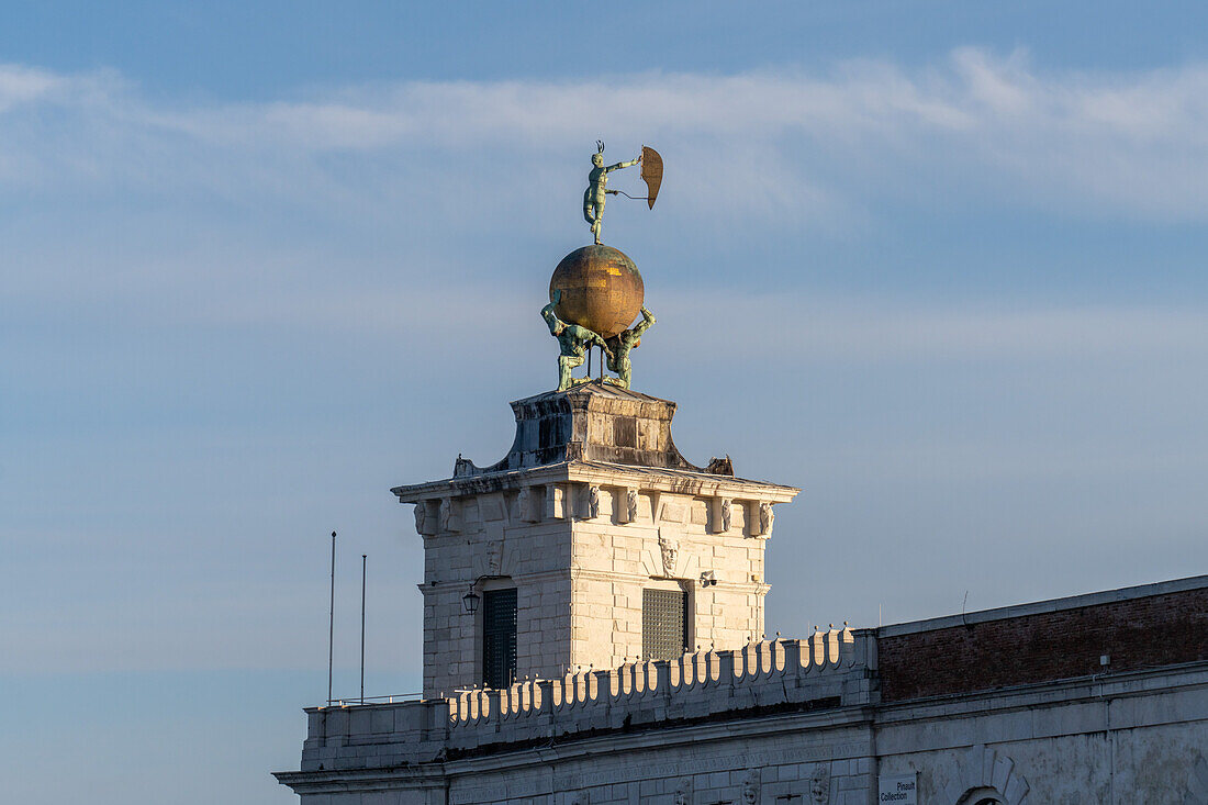 A statue on the point of Punta della Dogana in Venice, Italy. Two atlases supporting a gilded globe with a weathervane representing Fortuna, completed in 1677 by Bernardo Falcone.