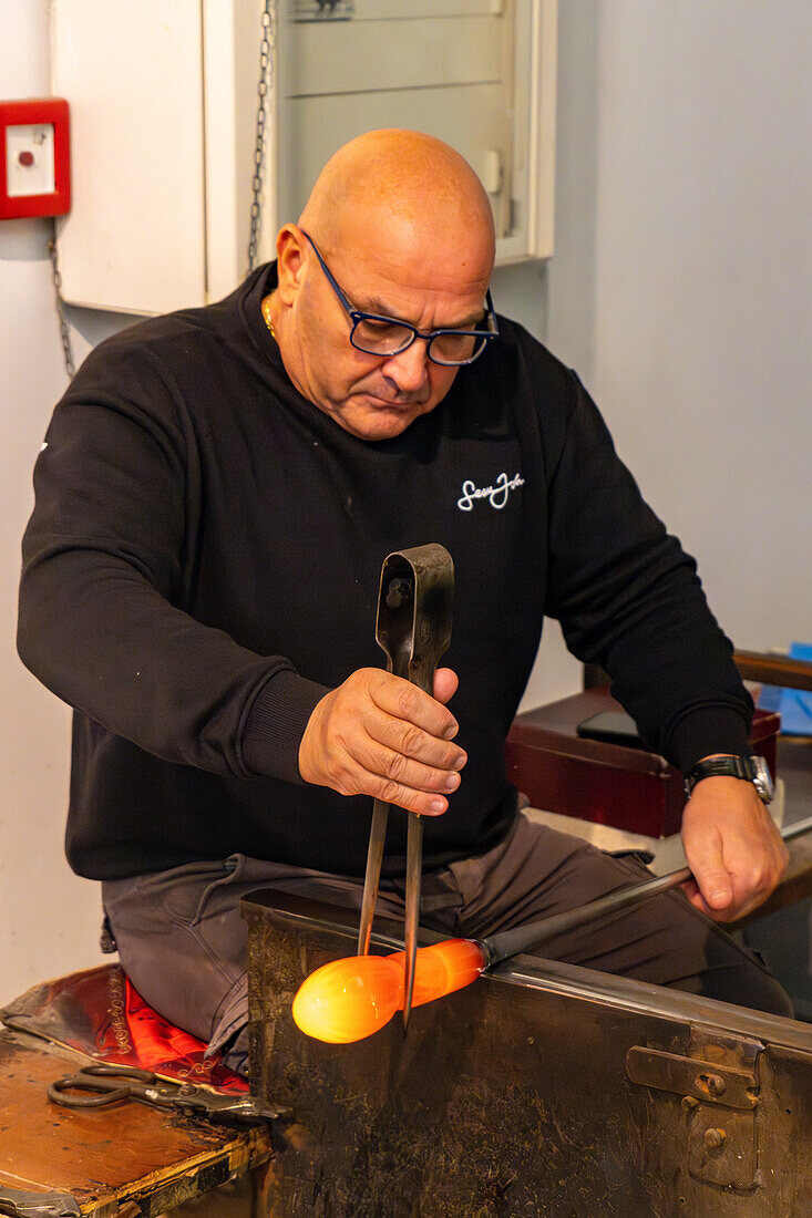 The glassblower shapes the molten glass with jacks in a glassblowing demonstration in Venice, Italy.