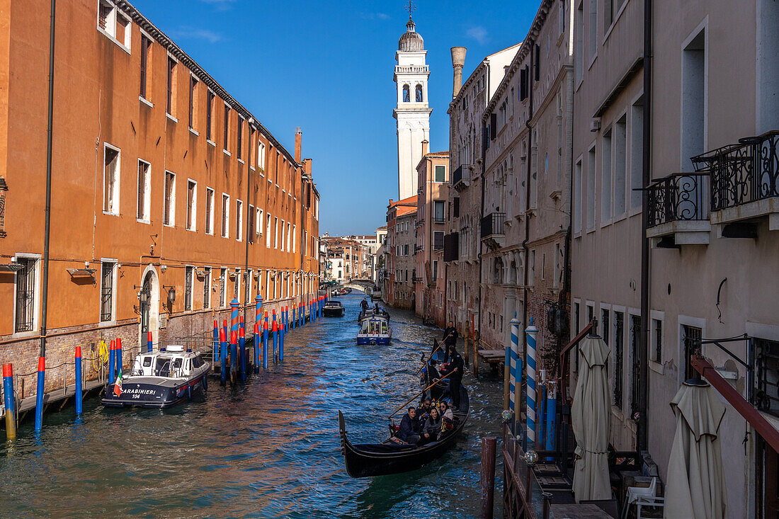 Two gondolas carrying tourists in a canal in Venice, Italy. Behind is the leaning bell tower or campanile of the Greek Orthodox Church of San Giorgio dei Greci.