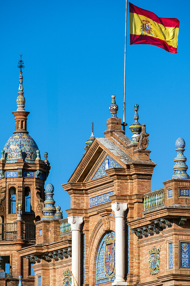 Close up of the intricate architectural details of Plaza de España in Seville, Spain, featuring traditional Spanish design elements and a vibrant flag against a clear blue sky.