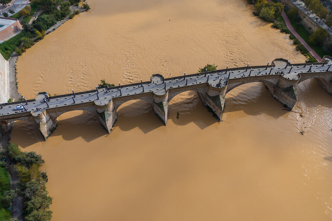 Aerial view of an abundant Ebro River passing under the Stone Bridge after the Dana, Zaragoza, Spain