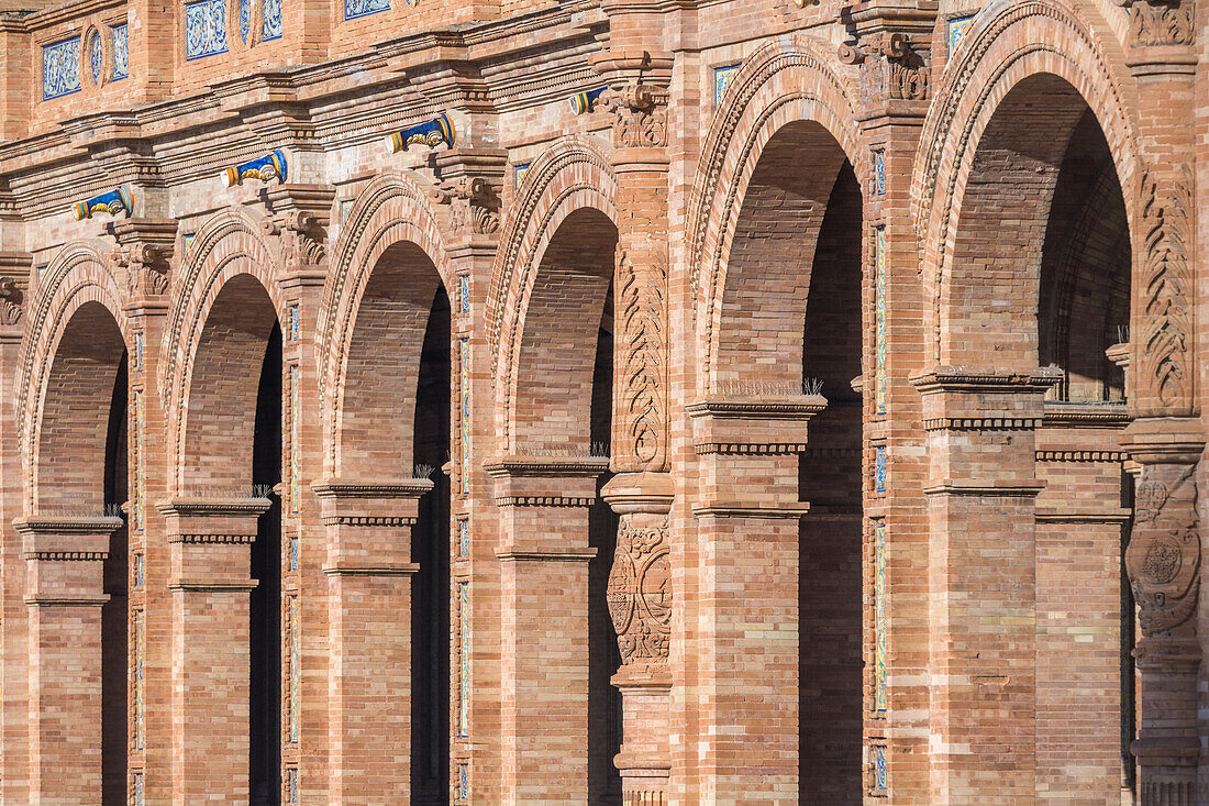 Nahaufnahme der kunstvollen Backsteinbögen auf der Plaza de España in Sevilla,Spanien,mit komplizierten architektonischen Details und schattenwerfendem Sonnenlicht. Ein Meisterwerk der spanischen Renaissance-Architektur.