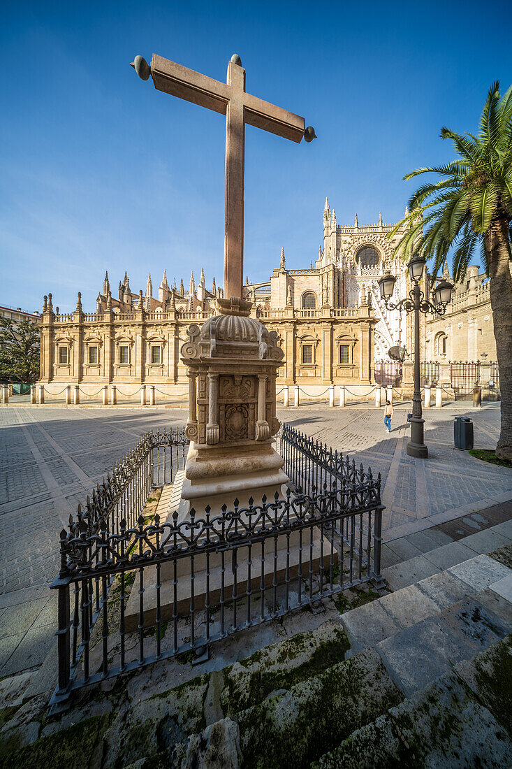 Cruz de los Juramentos and Cathedral of Seville under clear blue sky.