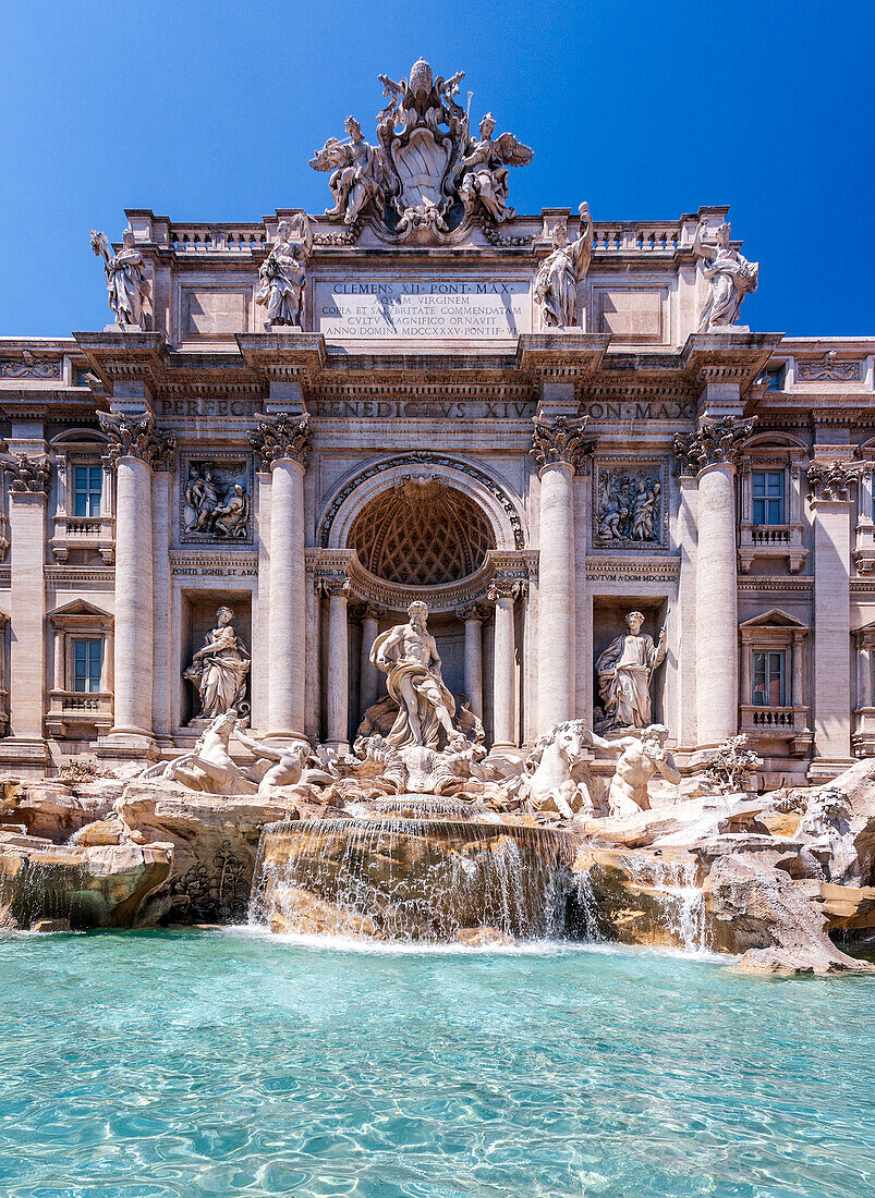 Besucher bewundern die Erhabenheit des Trevi-Brunnens,dessen Wasser im Sonnenlicht vor einem wunderschönen blauen Himmel schimmert.