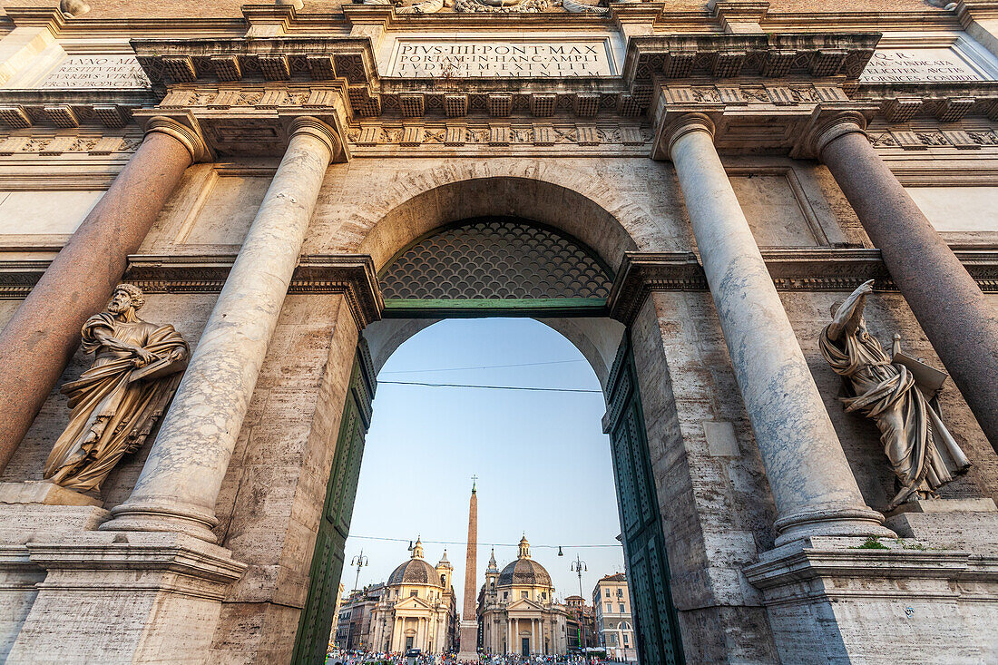 Porta del Popolo stands proudly, framing Piazza del Popolo under a clear blue sky in Rome, inviting visitors to explore the historical area.