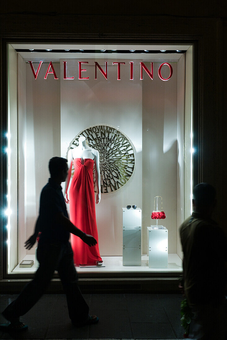 Rom,Italien,22. Juli 2017,Ein auffälliges rotes Kleid wird in einem Schaufenster in der Via Condotti ausgestellt und lockt abendliche Passanten in Rom an.