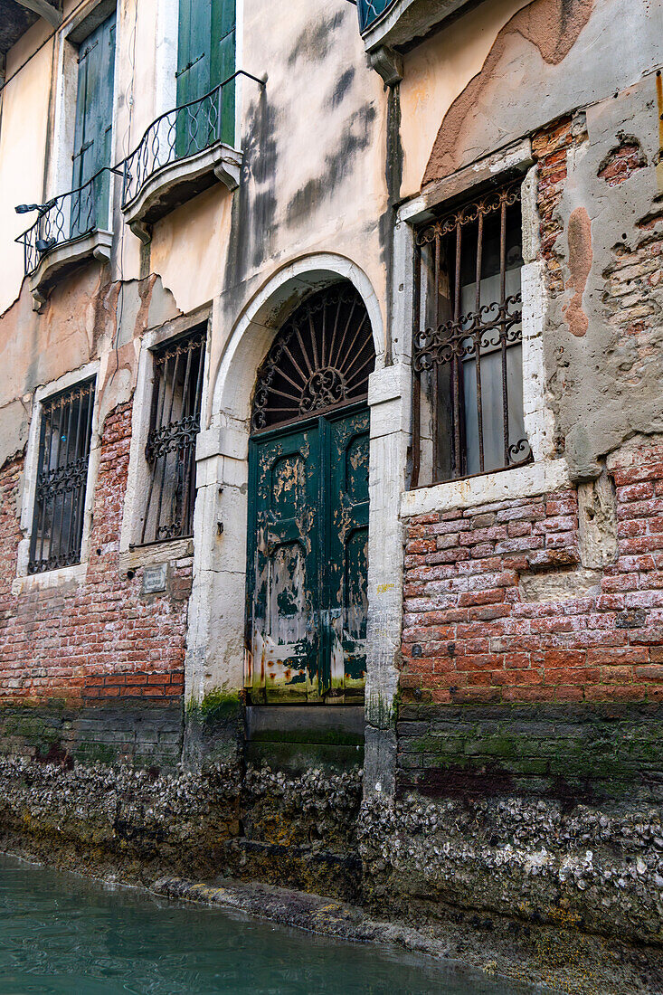 Doorway of a weathered building along a canal in Venice, Italy.