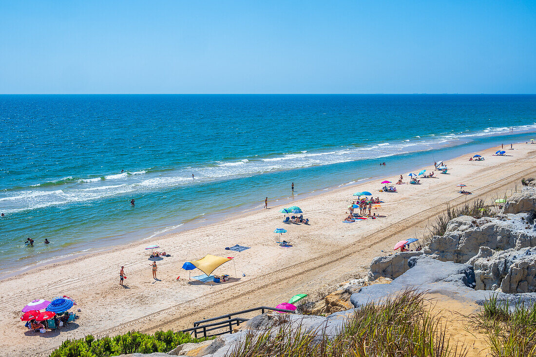 Relaxing view of Playa de Cuesta Maneli with vibrant umbrellas and sunbathers enjoying the sunny coastline in Huelva, Andalucia, Spain. Ideal for vacation and summer themes.