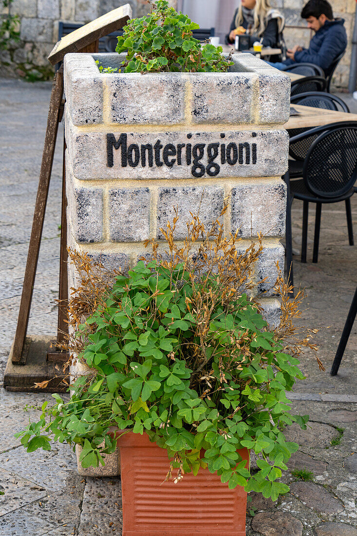 Ein Metallschild auf einem steinernen Blumenkasten in der mittelalterlichen Stadt Monteriggioni,Provinz Siena,Italien.