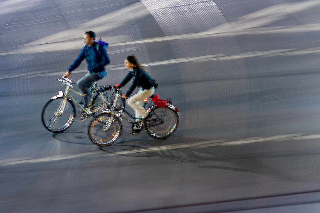 A dynamic image of a couple cycling through city streets at night. The motion blur captures a sense of speed and urban life.