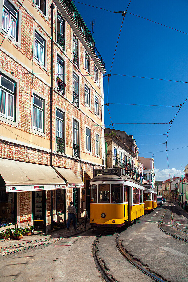 A bright yellow tram travels along Rua das Escolas Gerais in the charming Alfama district of Lisbon on a sunny day.