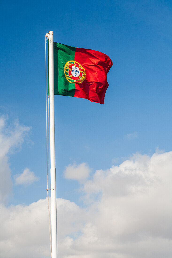 The vibrant Portuguese flag flutters against a bright blue sky, showcasing Lisbon's beauty and cultural pride.