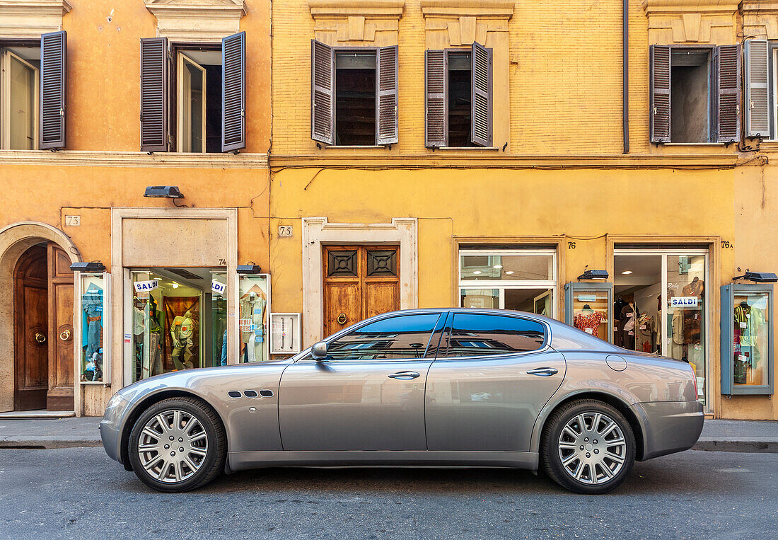 A sleek luxury sedan sits parked outside a boutique on Via Frattina in central Rome, showcasing the city's stylish atmosphere.