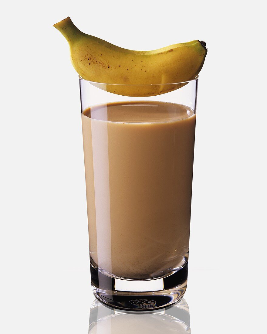A glass of banana and coffee milk, a baby banana on top