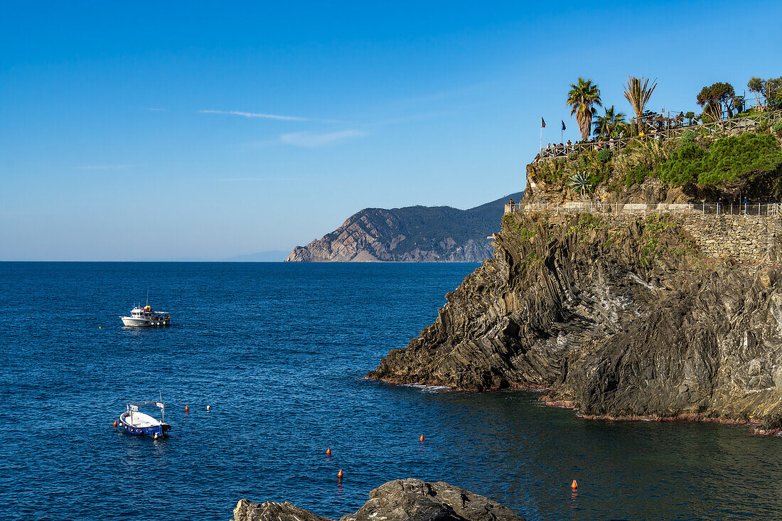 Fishing boats off the rugged coast of the Cinque Terre town of Manarola, Italy. Tourists are on an overlook at right.