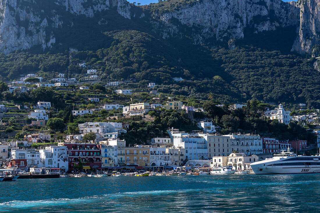 Blick von einem Boot auf den Hafen und die Uferpromenade von Marina Grande auf der Insel Capri, Italien. Rechts ist eine große Hochgeschwindigkeits-Passagierfähre zu sehen.