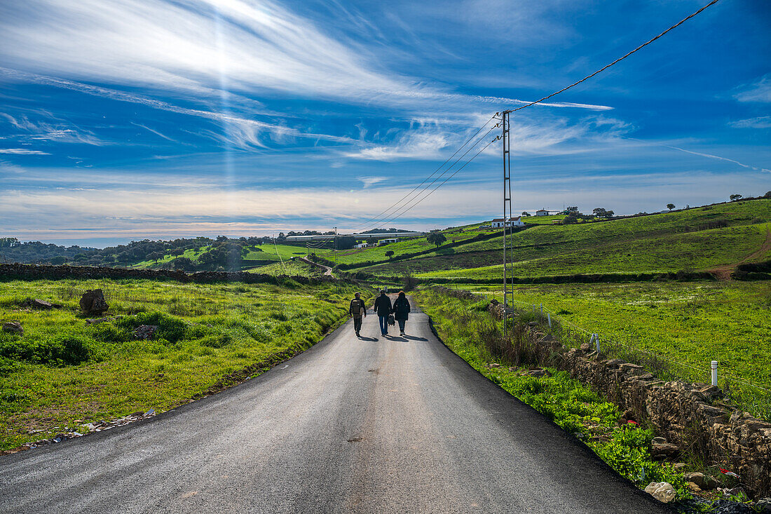 People walking a scenic rural road with a green landscape in Alosno, Spain