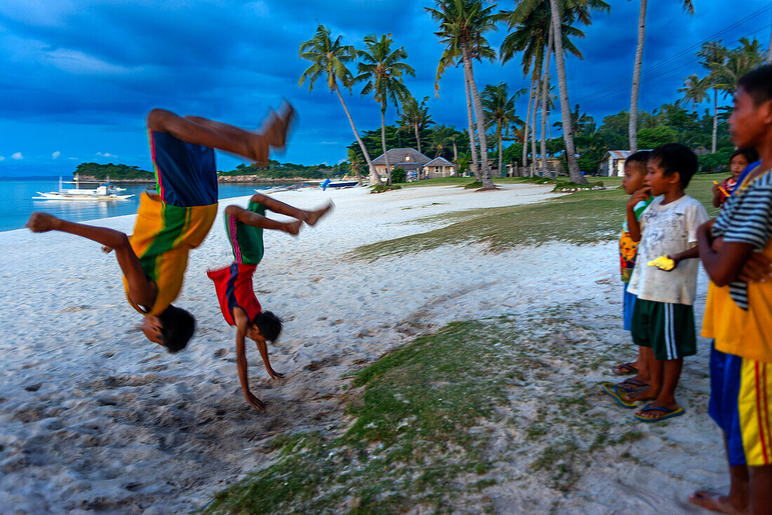 Local children doing stunts in the white sand beach of Langub Beach in Malapascua island, Cebu, Philippines