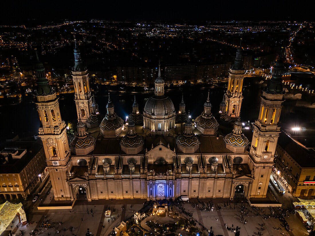 Luftaufnahme der Kathedralenbasilika Unserer Lieben Frau von der Säule und des nachts beleuchteten Platzes El Pilar während der Weihnachtszeit, Zaragoza, Spanien