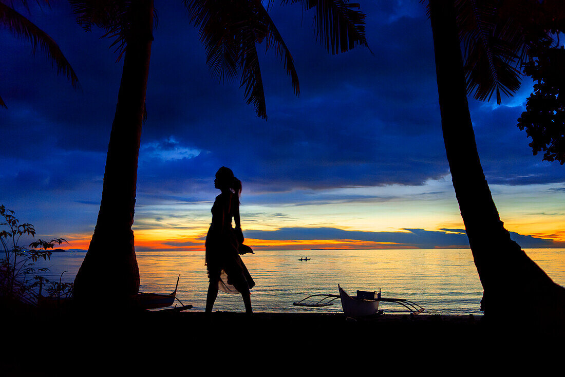 Einheimische Frau im Sonnenuntergang am weißen Sandstrand von Langub auf der Insel Malapascua, Cebu, Philippinen