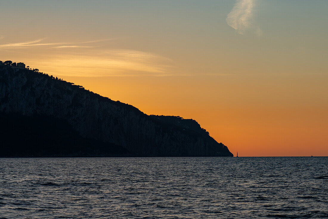 A sailboat at sunset in the Tyrrhenian Sea off the coast of the island of Capri in the Bay of Naples, Italy.